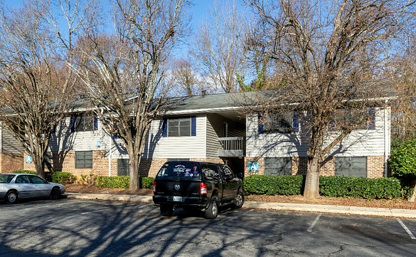 Charming apartment complex with cozy two-story units surrounded by lush greenery and convenient parking.