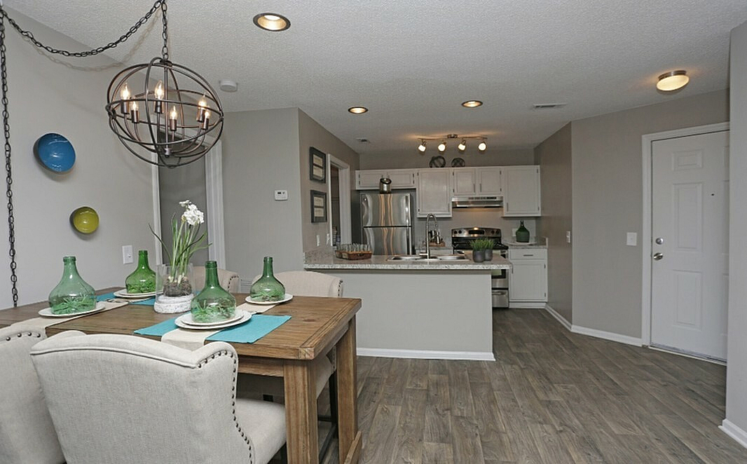 Chic open-concept kitchen and dining area with stylish lighting, rustic wooden table, and modern appliances.