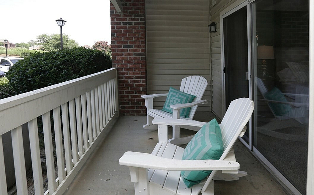 Charming apartment balcony with cozy white Adirondack chairs and vibrant teal cushions, offering a relaxing outdoor retreat.