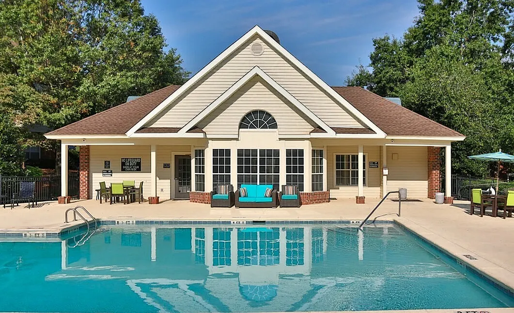 Charming clubhouse with inviting pool and cozy outdoor seating, surrounded by lush greenery for a serene living experience.