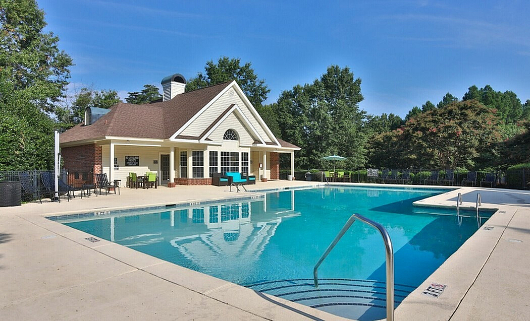 Inviting outdoor pool area with a charming clubhouse and lush greenery, perfect for relaxation and leisure.