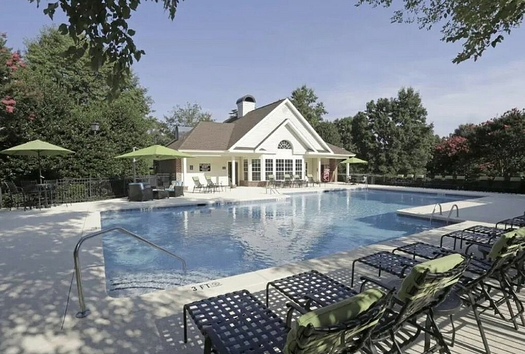 Inviting outdoor pool area with cozy lounge chairs and elegant clubhouse surrounded by lush greenery.