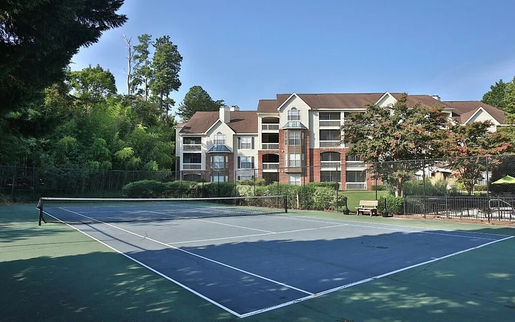 Elegant apartment complex with lush greenery and a well-maintained tennis court, perfect for active living.