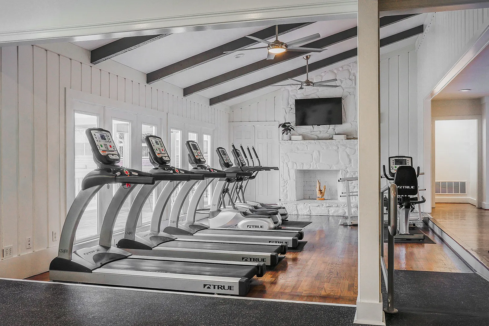 Elegant fitness room with modern treadmills, vaulted ceiling, stone fireplace, and vibrant teal walls.Elegant fitness room with modern treadmills, vaulted ceiling, stone fireplace, and vibrant teal walls.