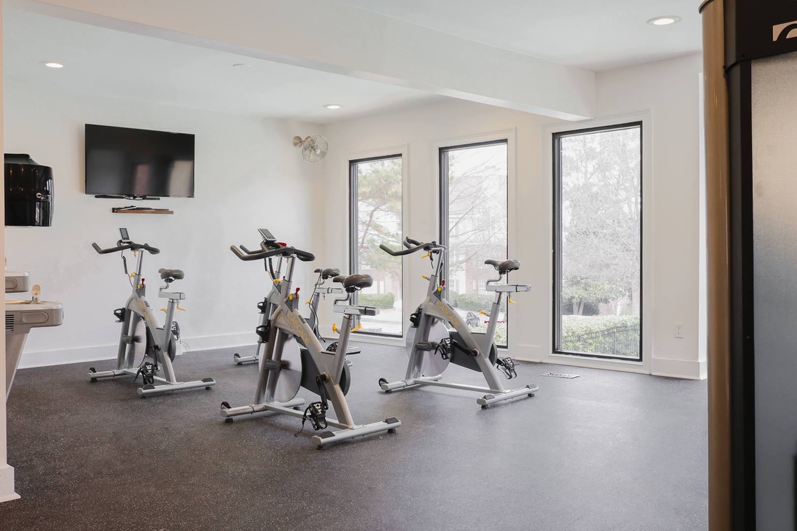 Modern fitness room with bright natural light featuring stationary bikes and a wall-mounted TV for an invigorating workout experience.