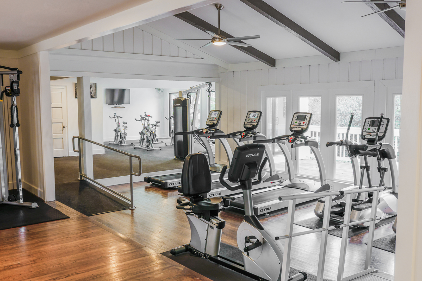 Modern apartment gym with state-of-the-art equipment, treadmills overlooking scenic views, and high ceilings with stylish beams.