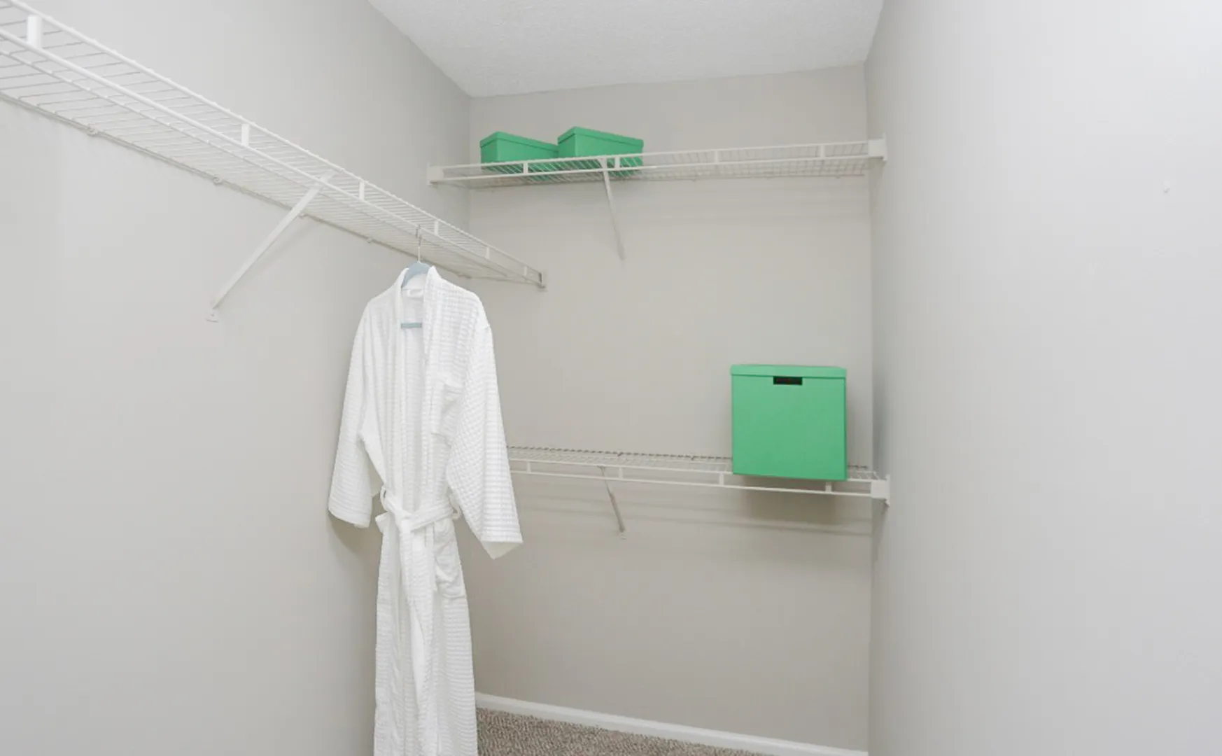 Spacious walk-in closet with ample shelving, featuring a plush white robe and vibrant green storage boxes for stylish organization.