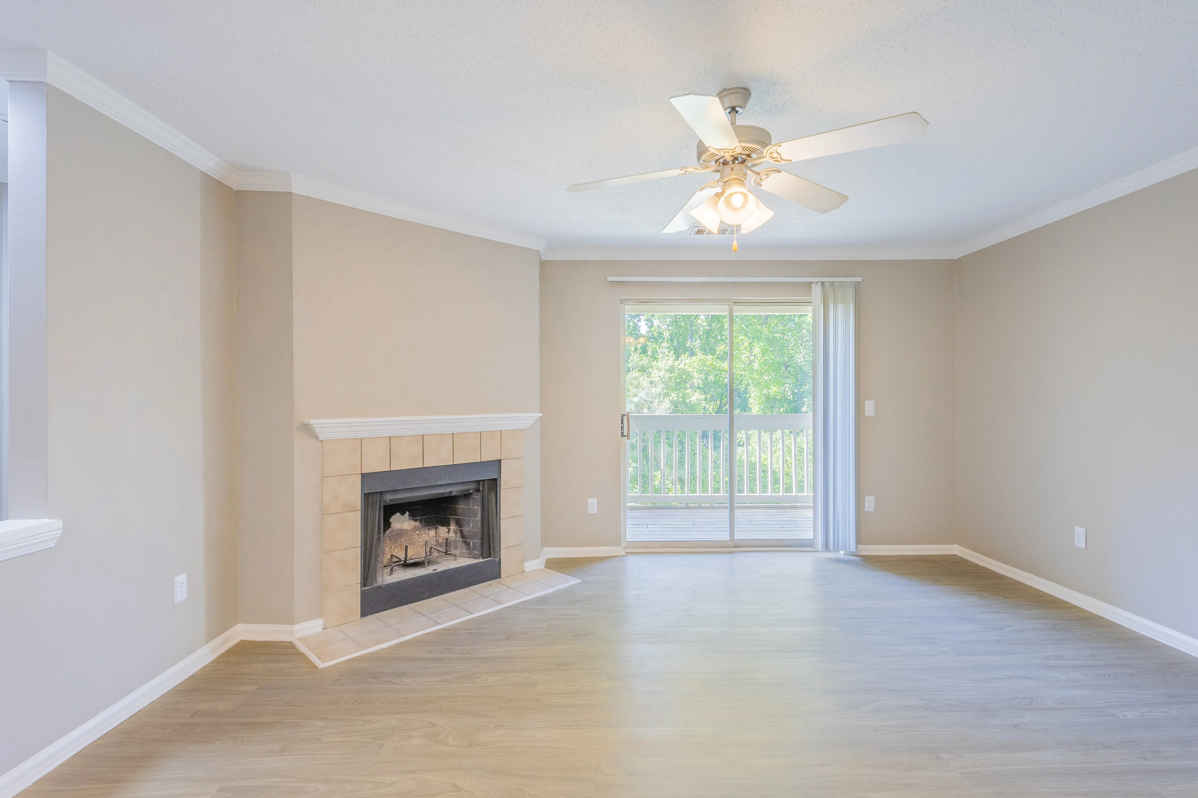 Bright living room with elegant wooden flooring, a cozy fireplace, and large sliding doors opening to a lush green view.