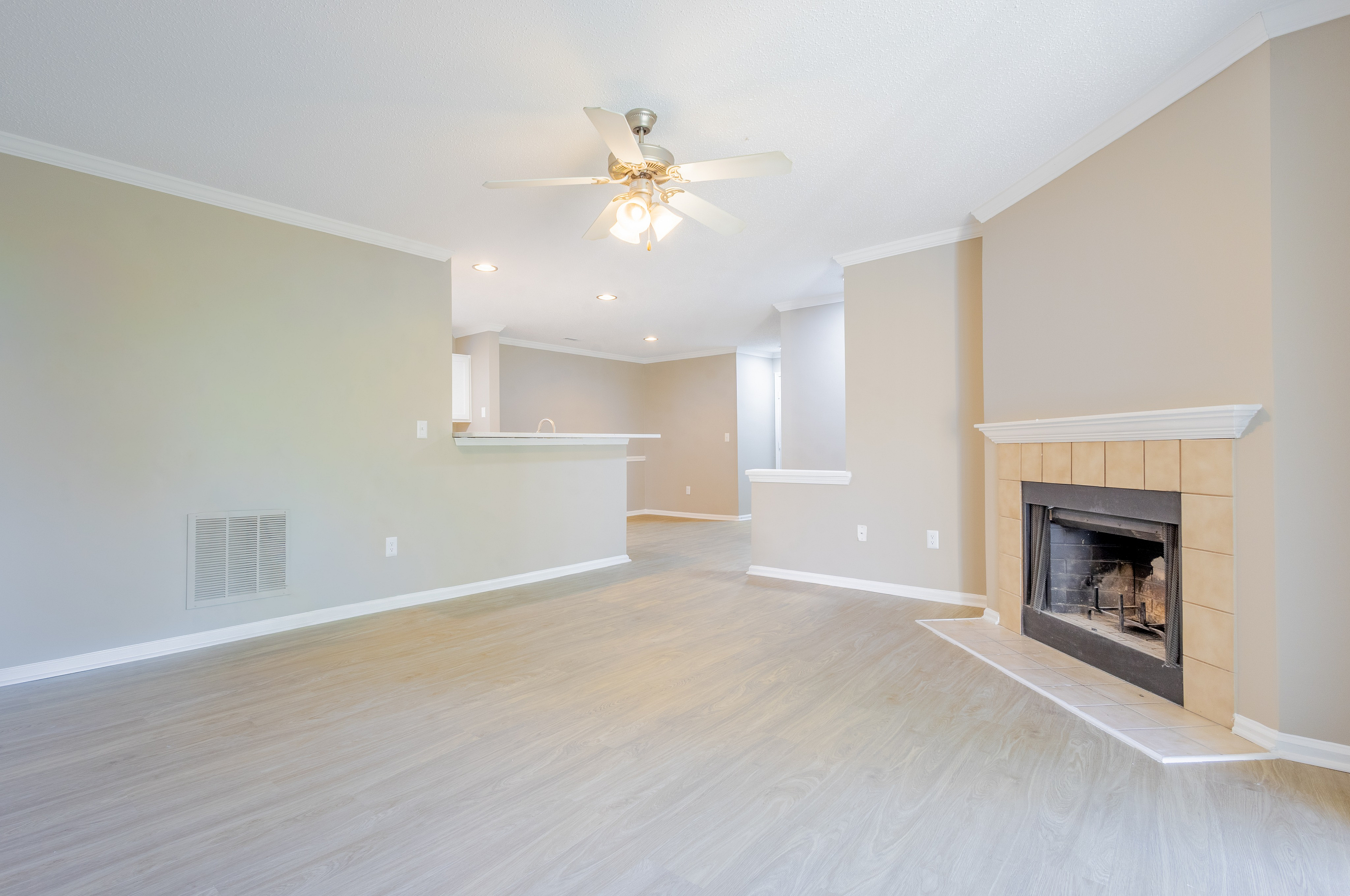 Bright and inviting living room with elegant fireplace, ceiling fan, and open-concept layout leading to a modern kitchen.