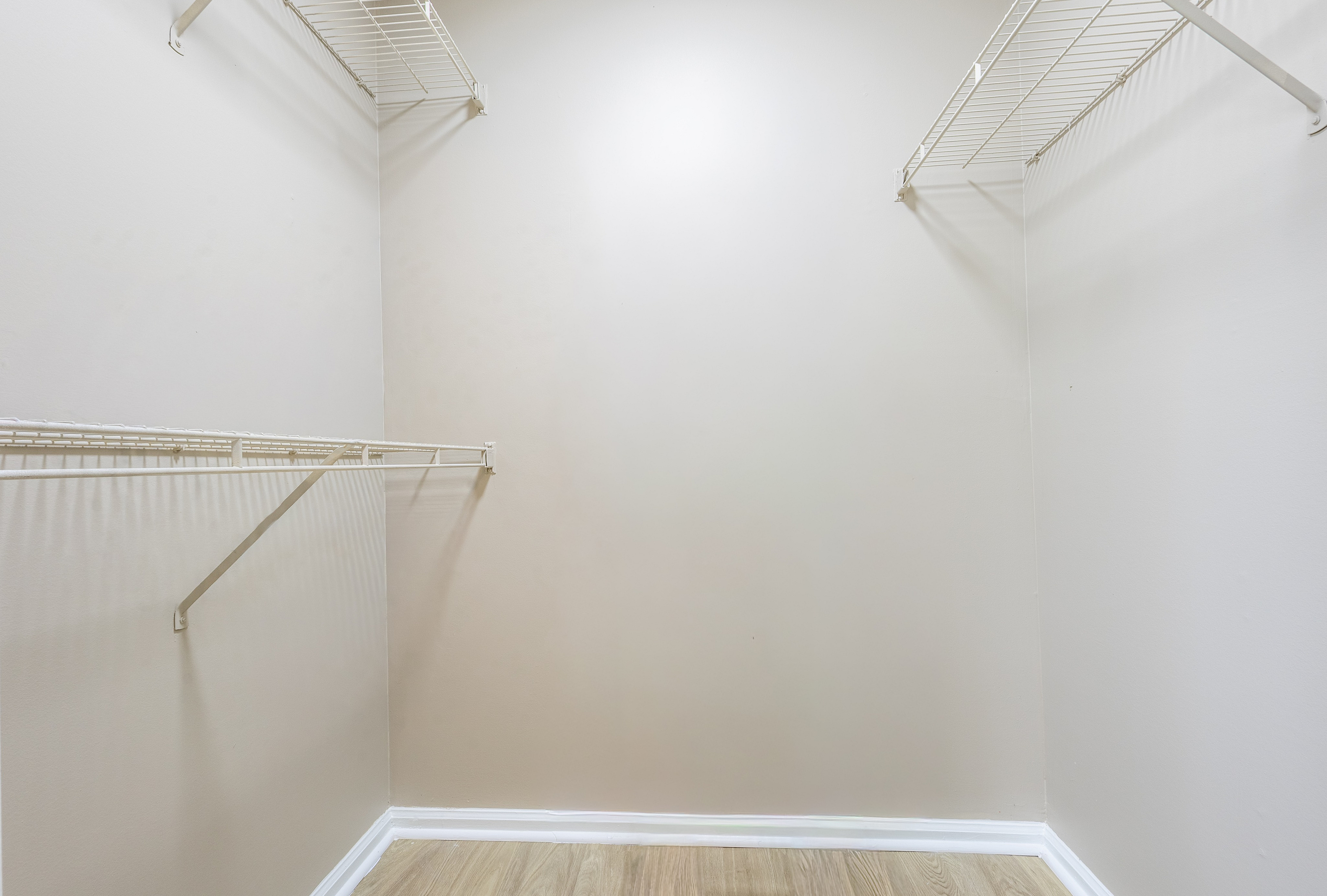 Spacious walk-in closet with sleek wire shelving and stylish hardwood flooring, perfect for ample storage and organization.