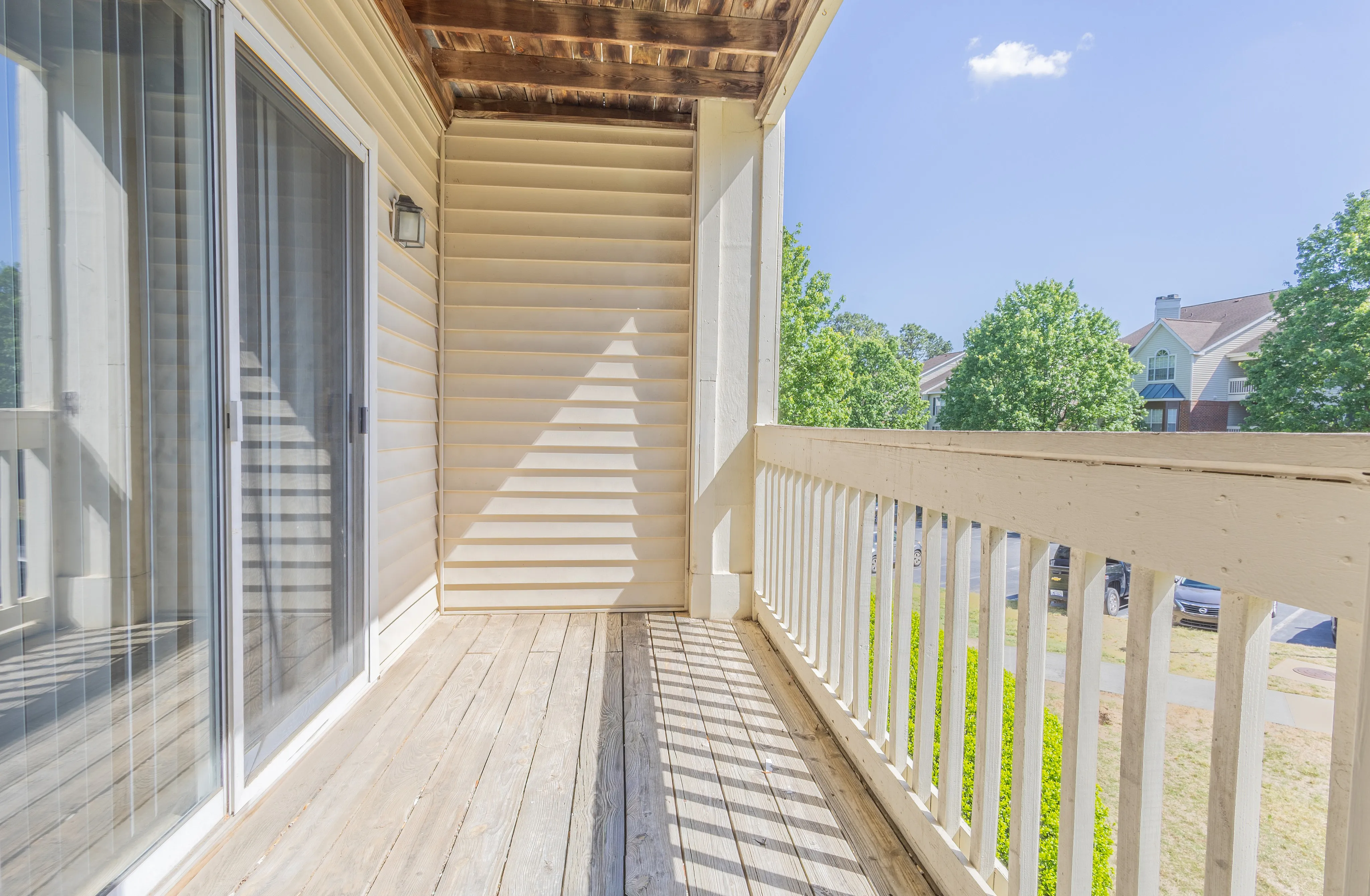 Bright and airy balcony with wooden decking, featuring elegant white railings and a view of lush green trees.