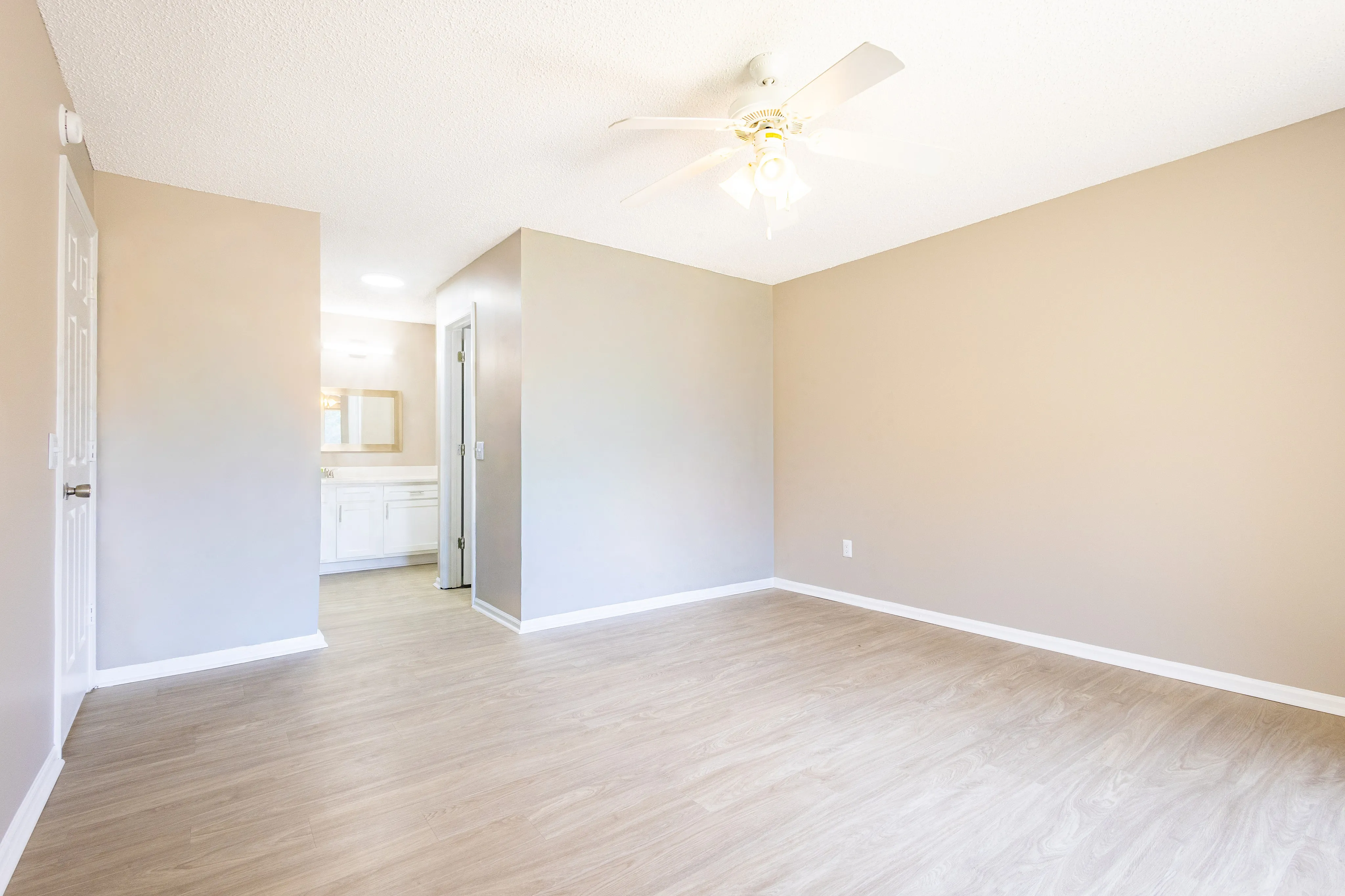Bright and spacious room with elegant wood flooring and modern ceiling fan, leading to a sleek bathroom with stylish fixtures.