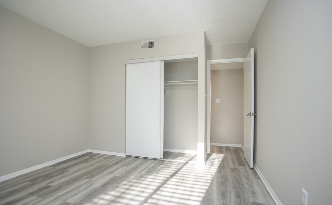 Bright, modern bedroom with sleek hardwood flooring and ample natural light, featuring a minimalist closet.