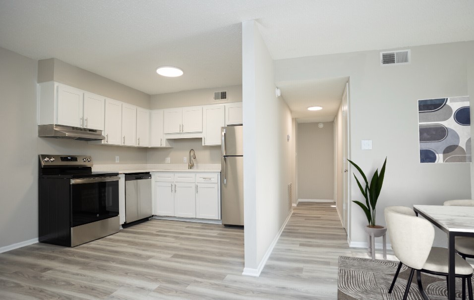 Modern kitchen with sleek white cabinetry, stainless steel appliances, and open layout leading to dining area. Perfect blend of elegance and functionality.