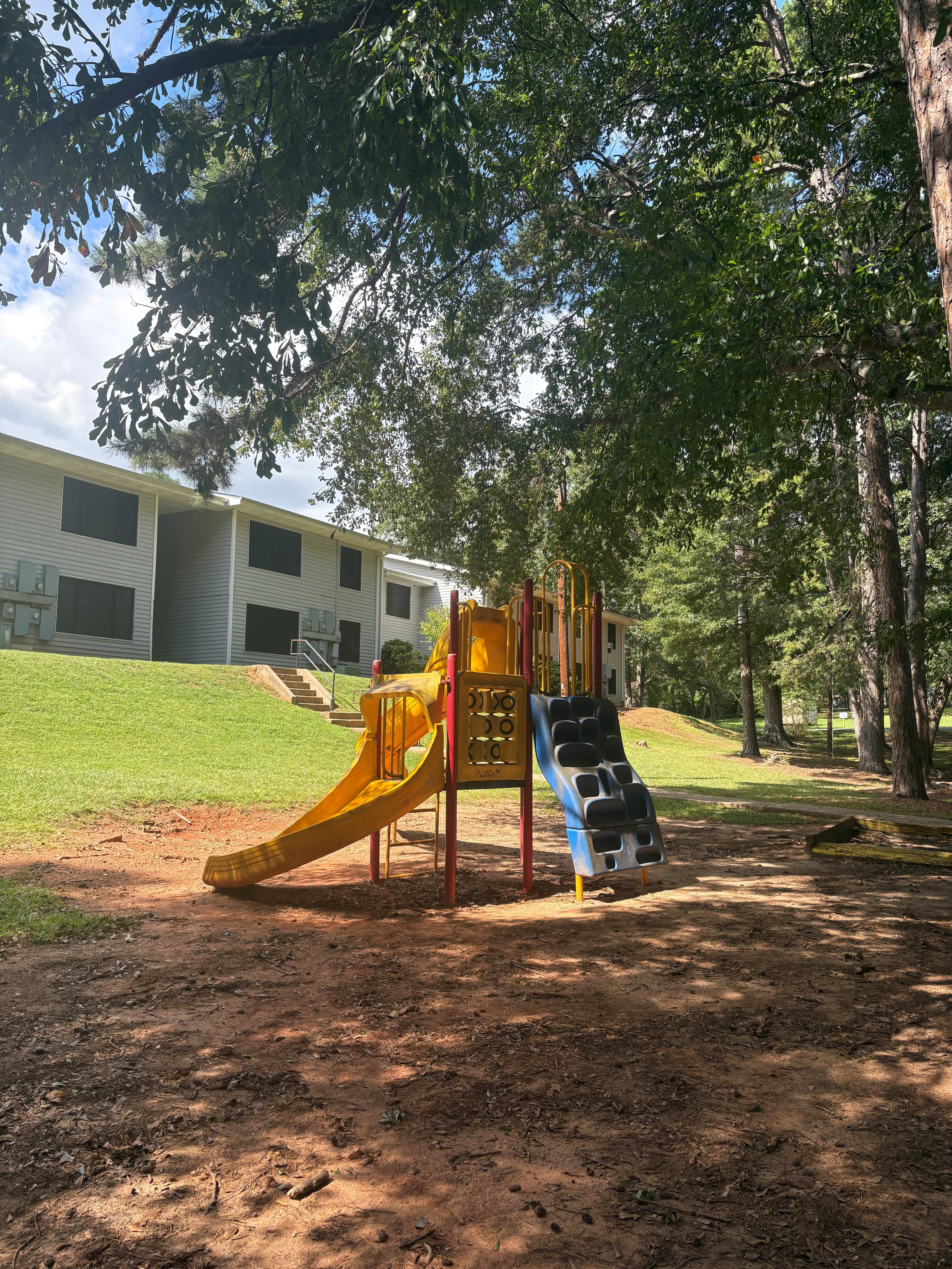 Charming apartment complex nestled amidst lush greenery, featuring a vibrant children\'s playground with slides for family enjoyment.