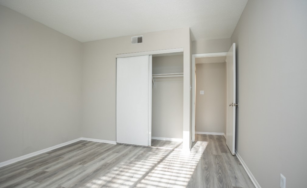 Bright, minimalist bedroom with sleek flooring and ample natural light, highlighting a spacious closet and neutral walls.