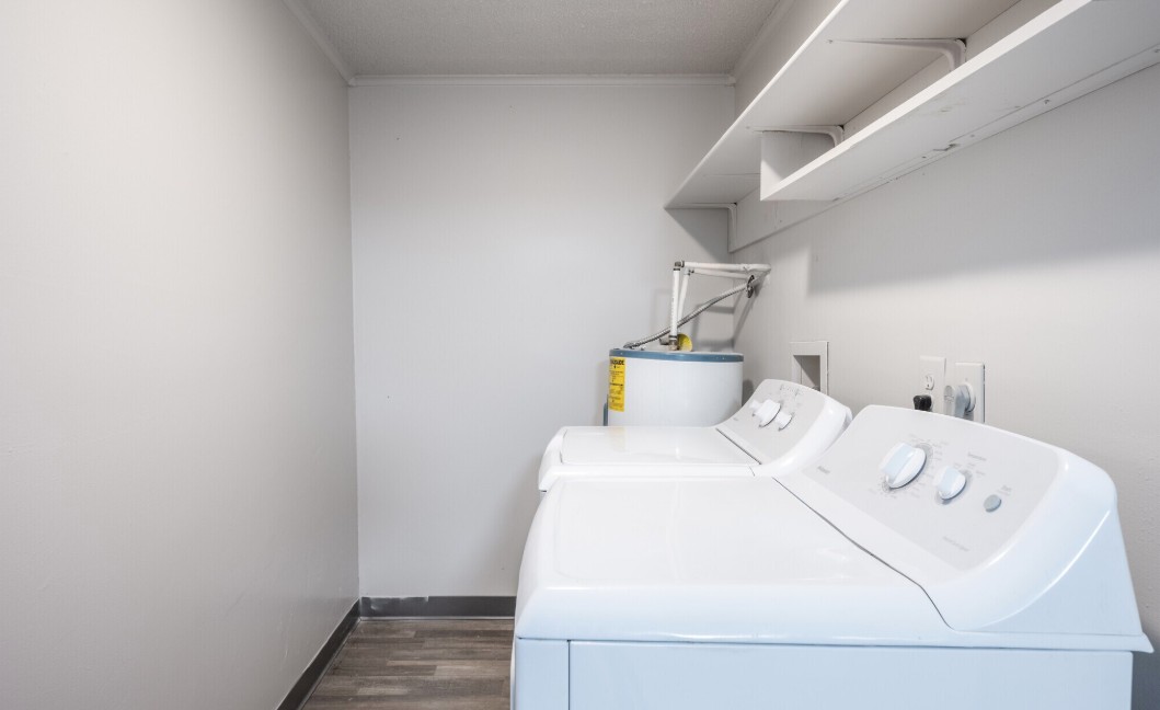 Bright and spacious laundry room with modern washer and dryer, ample shelving, and a water heater for convenience.