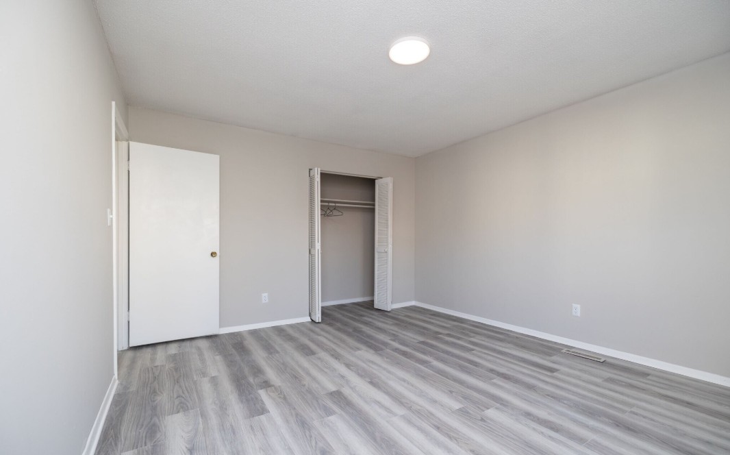 Bright and airy empty room with modern gray laminate flooring, neutral walls, and a spacious closet with white doors.