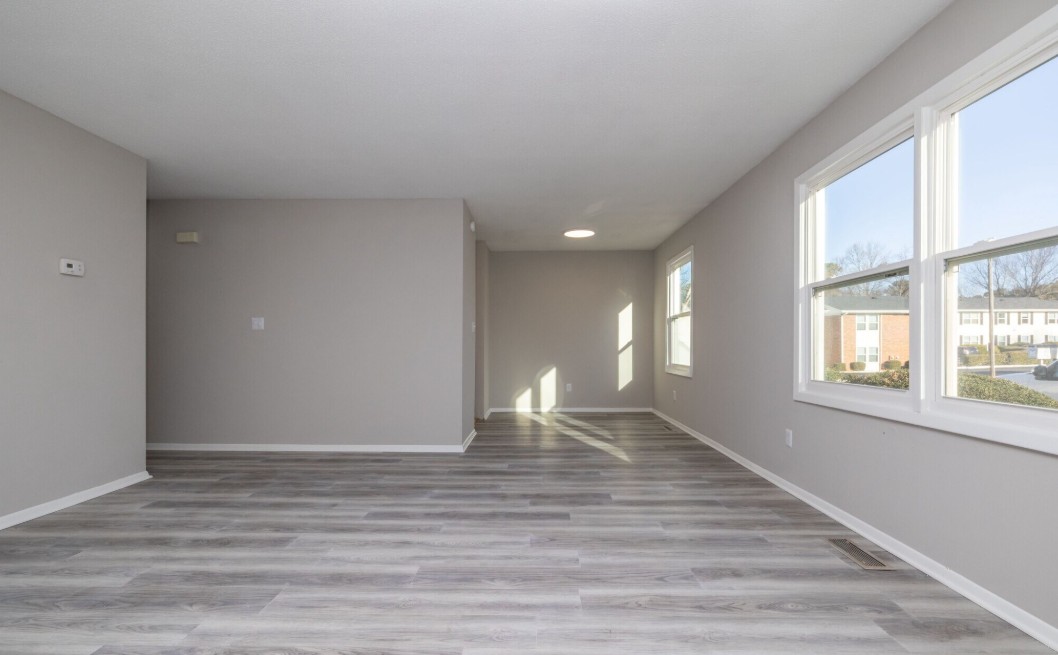 Bright and spacious living room with large windows, modern gray flooring, and neutral wall colors offering a blank canvas for personalization.