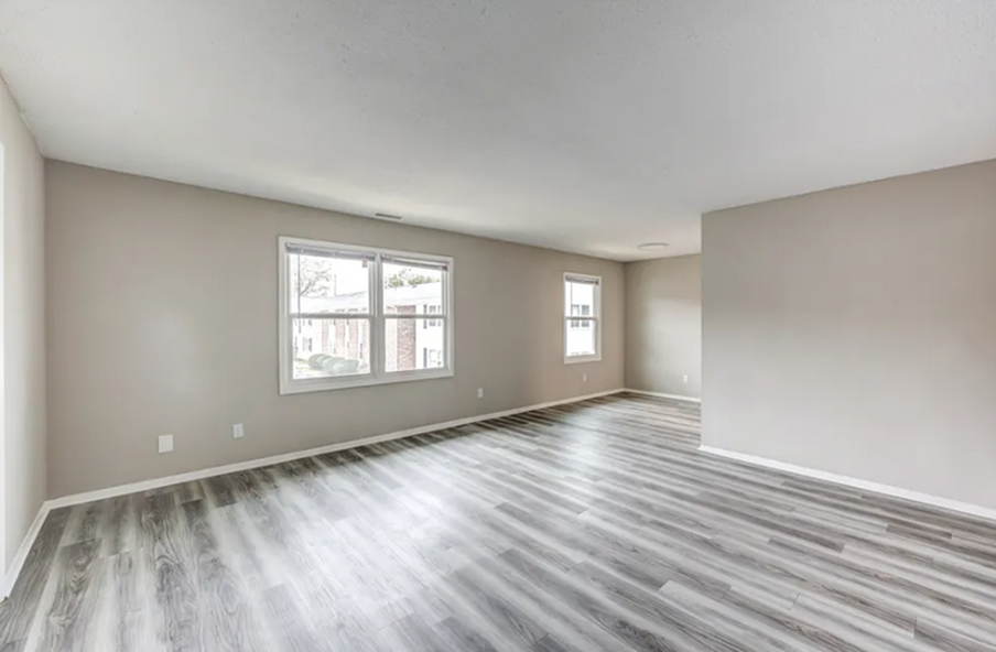 Spacious, light-filled living area with modern wood flooring, featuring neutral gray walls and large windows for natural illumination.