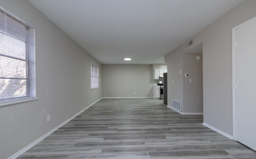 Bright and spacious open-plan living area with elegant wood flooring, large windows, and modern kitchen in the background.