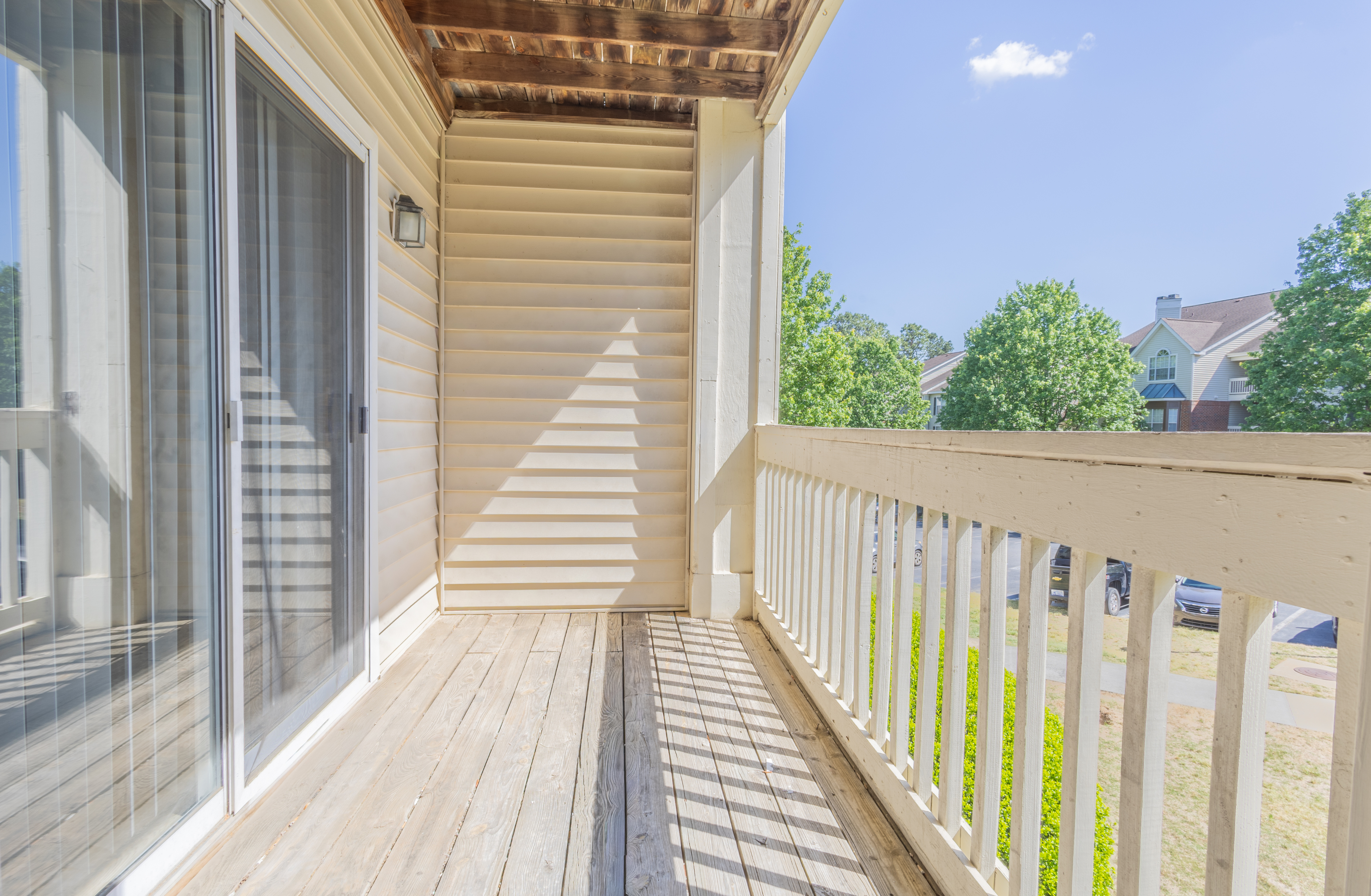 Inviting balcony with charming wooden flooring, sliding glass door, and a scenic view of lush green trees and neighborhood buildings.
