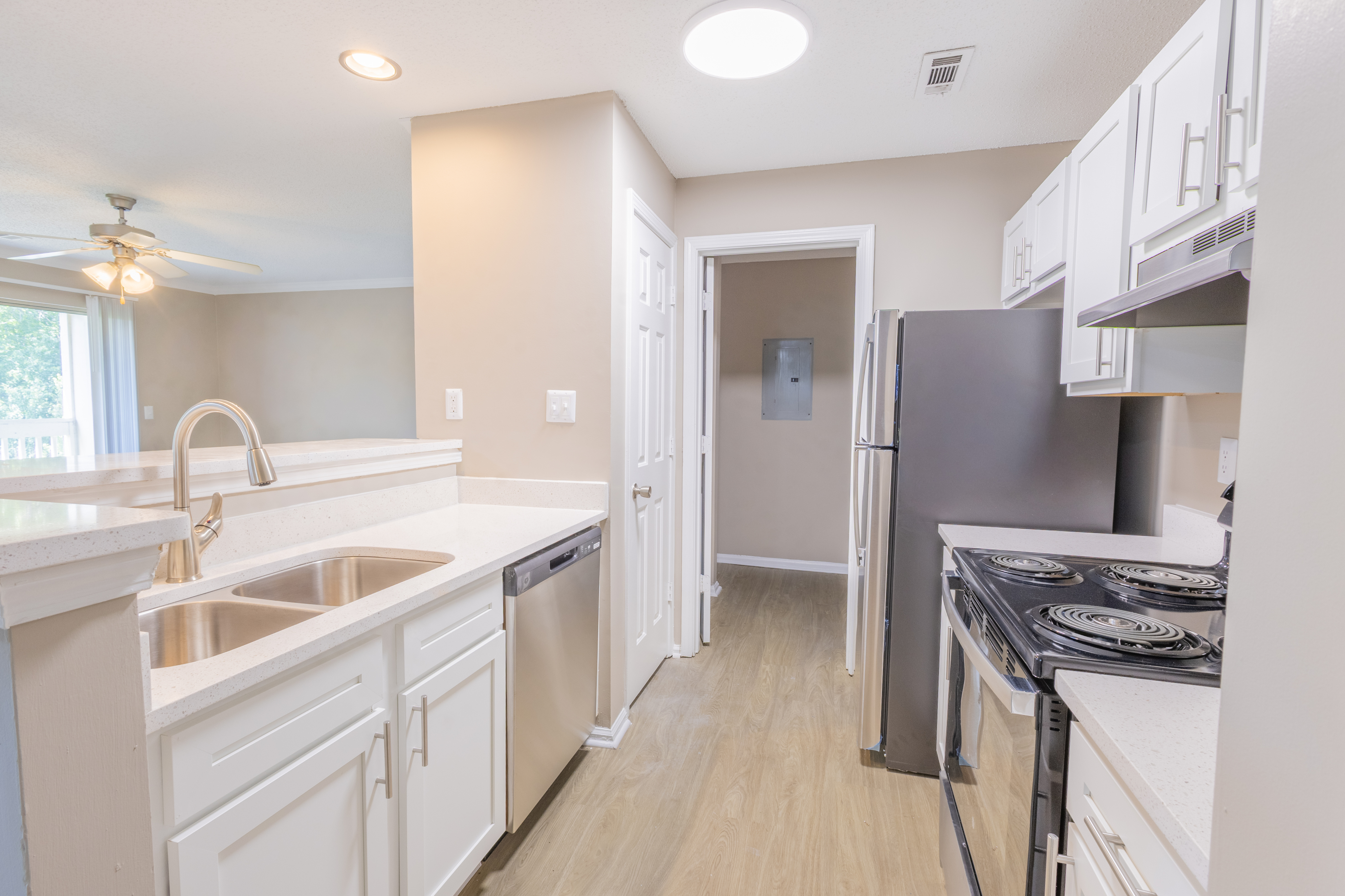 Bright and airy kitchen with sleek stainless steel appliances, modern cabinetry, and elegant countertops flowing into an inviting living area with ceiling fan.