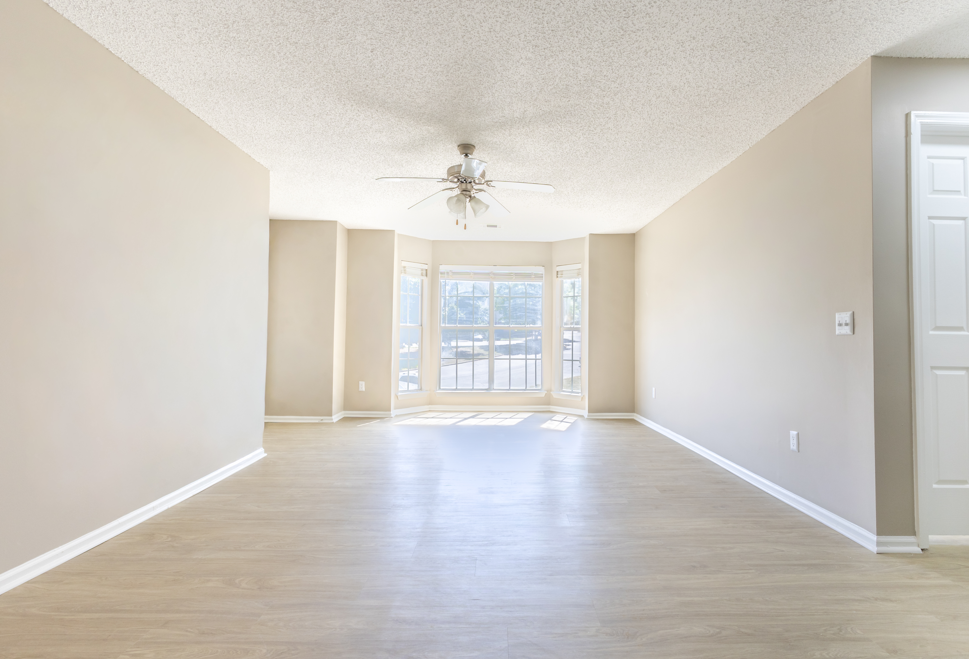 Bright and spacious living area with elegant hardwood floors, large bay windows, and a central ceiling fan, perfect for showcasing natural light.