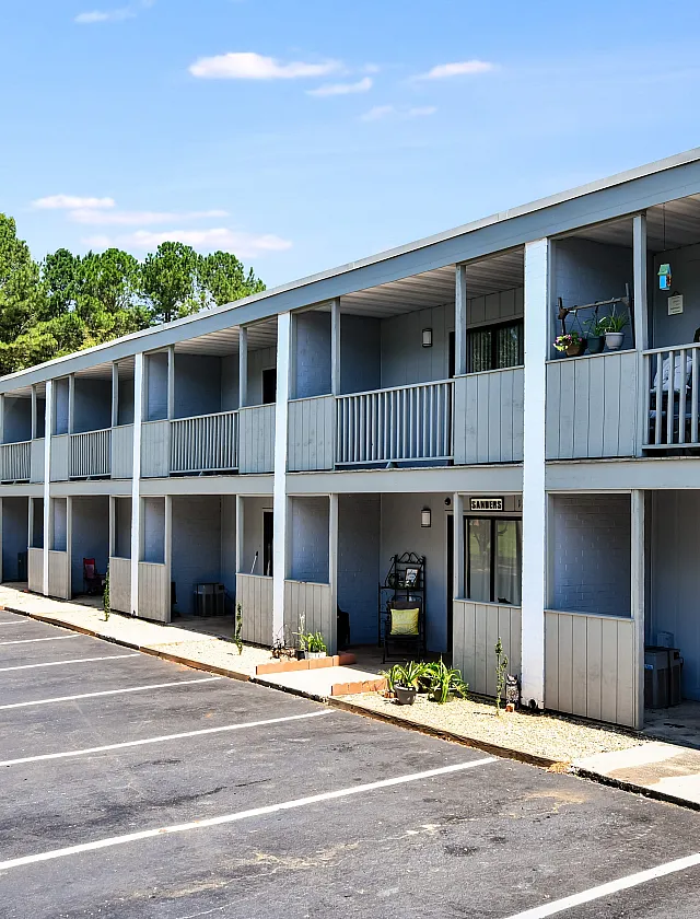 Charming two-story apartment complex with spacious balconies and ample parking, set against a backdrop of lush greenery.