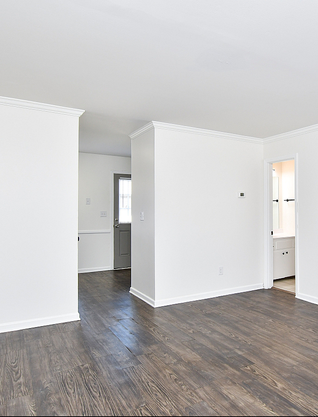 Bright minimalist apartment interior featuring elegant dark hardwood floors against crisp white walls, leading to a modern bathroom through a sleek doorway.