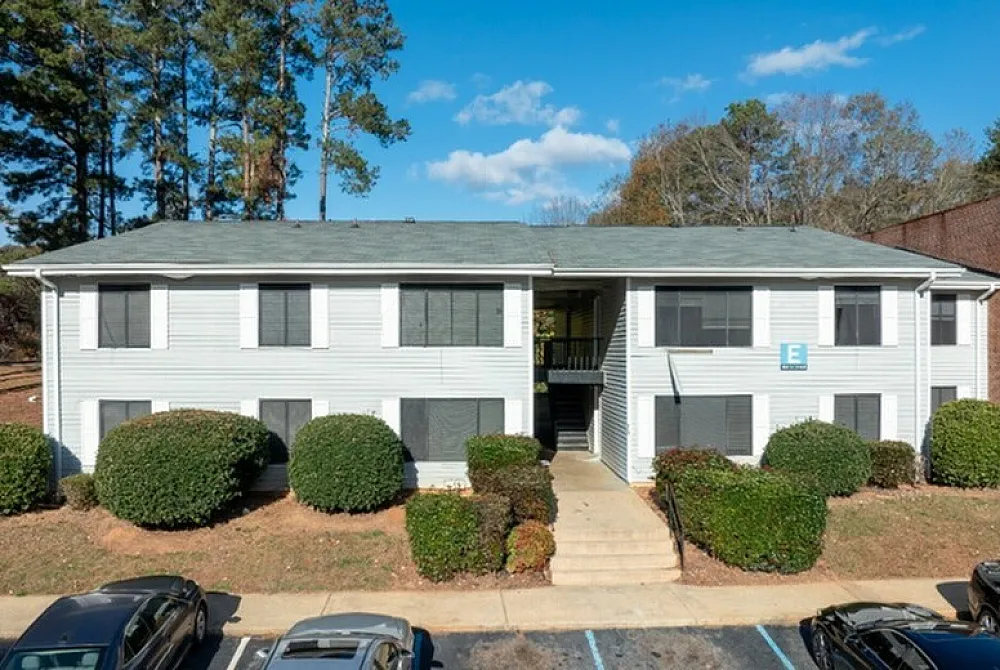 Charming two-story apartment building with well-maintained gardens and ample parking, nestled in a tranquil neighborhood surrounded by lush trees.