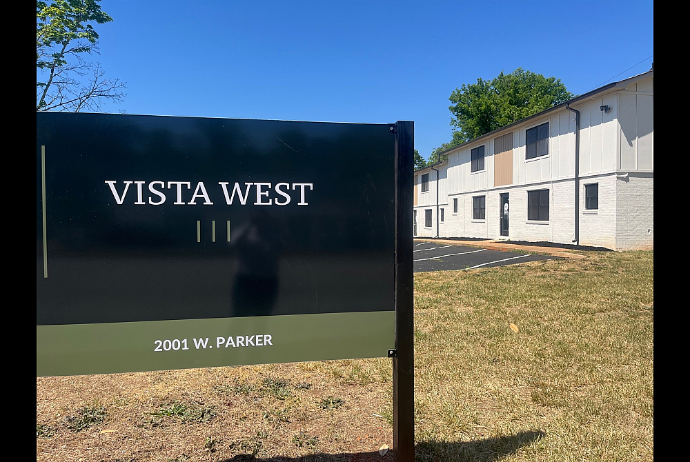 Vista West apartment complex with modern architecture, surrounded by lush greenery under a clear blue sky.