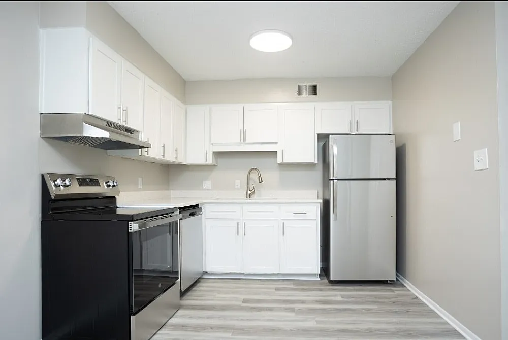 Modern kitchen with sleek stainless steel appliances, pristine white cabinetry, and elegant wood flooring.