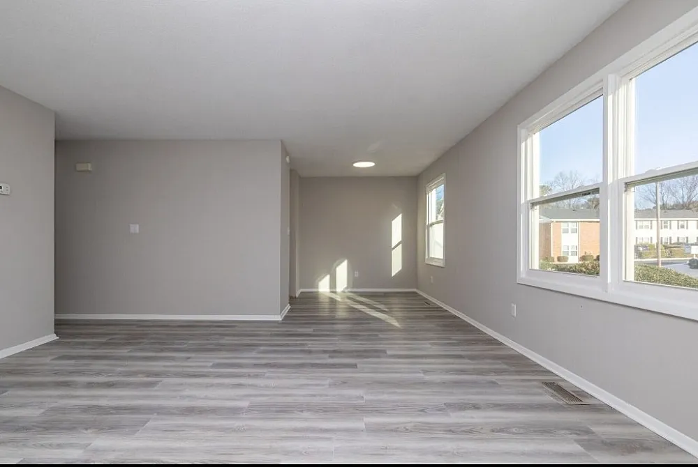 Bright, spacious living area with elegant gray flooring and abundant natural light from large windows.