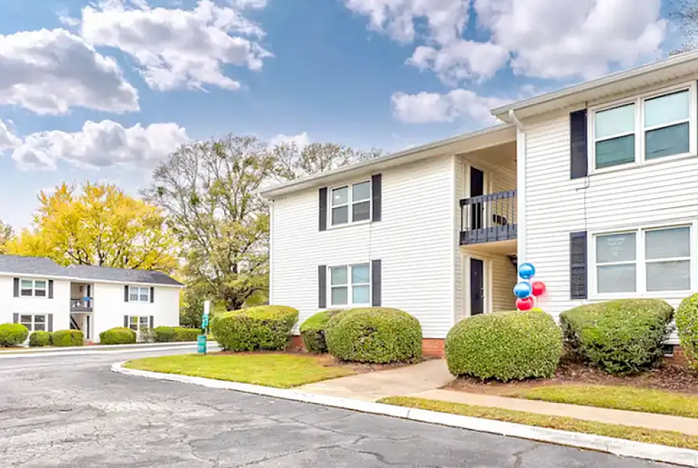 Charming apartment exterior with vibrant landscaping, elegant balcony, and welcoming neighborhood vibe under a picturesque sky.