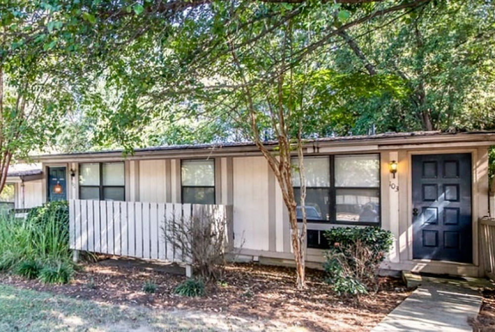 Charming single-story house with a contemporary facade, surrounded by lush green trees, featuring large windows and a welcoming front door.