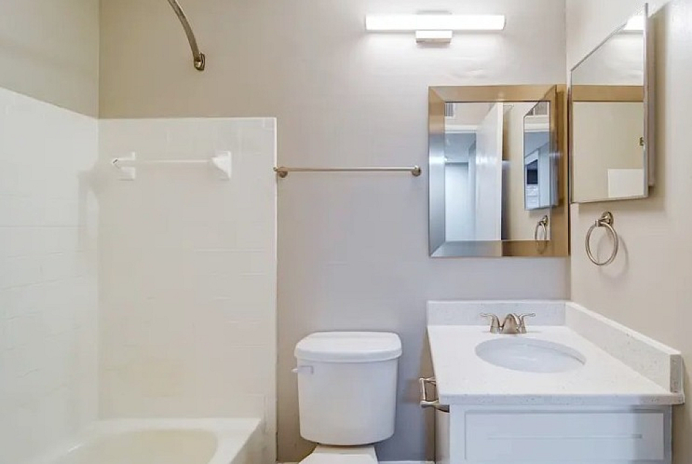 Bright and modern bathroom featuring a sleek vanity, elegant framed mirror, and pristine bathtub with stylish fixtures.