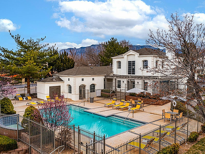 Inviting apartment complex with a sparkling outdoor pool, surrounded by lush landscaping and vibrant yellow lounge chairs, set against a backdrop of beautiful mountains.