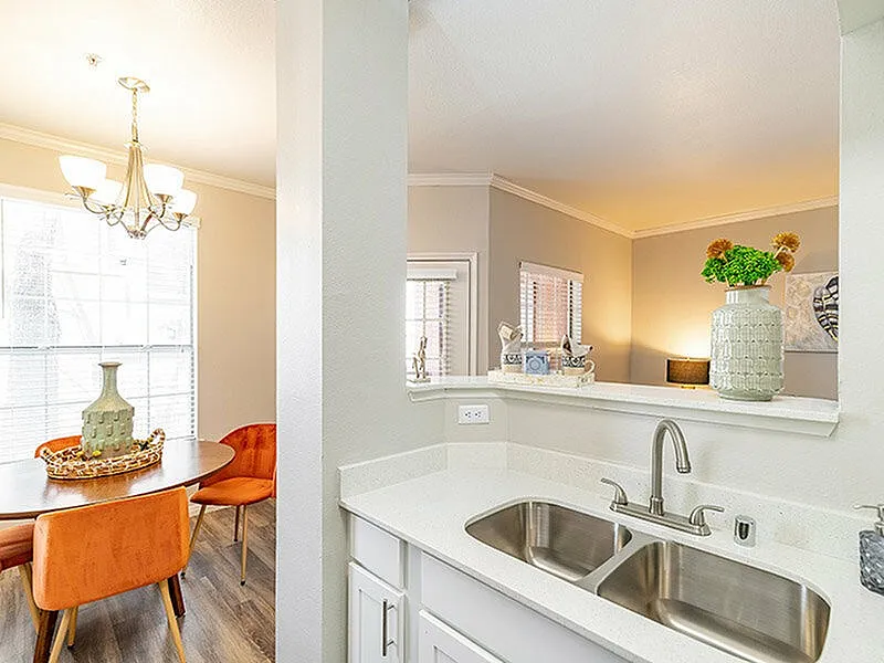 Elegant open-concept apartment kitchen with dual sinks, modern lighting, and cozy dining area adorned with vibrant orange chairs and decorative accents.