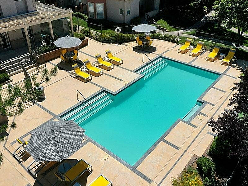 Luxurious apartment pool area with inviting turquoise water, surrounded by stylish yellow lounge chairs and elegant umbrellas, creating a perfect oasis for relaxation and sunbathing.