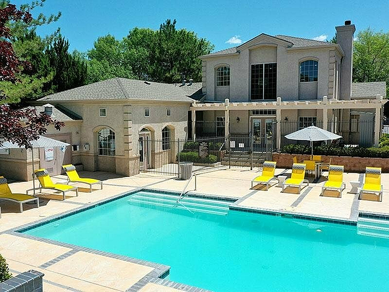 Charming apartment building with a luxurious pool surrounded by stylish yellow lounge chairs, offering a perfect blend of relaxation and elegance.