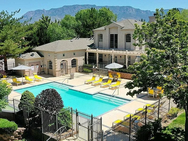 Luxurious apartment complex with inviting swimming pool, sun loungers, and mountain views surrounded by lush greenery.