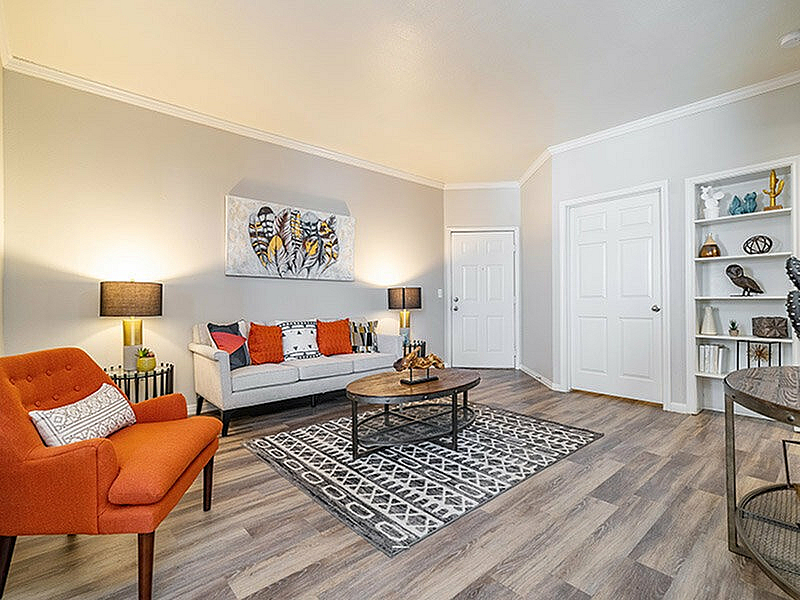 Inviting living room with modern decor, featuring a cozy orange armchair, stylish gray sofa with vibrant cushions, and chic coffee table set on a patterned rug.