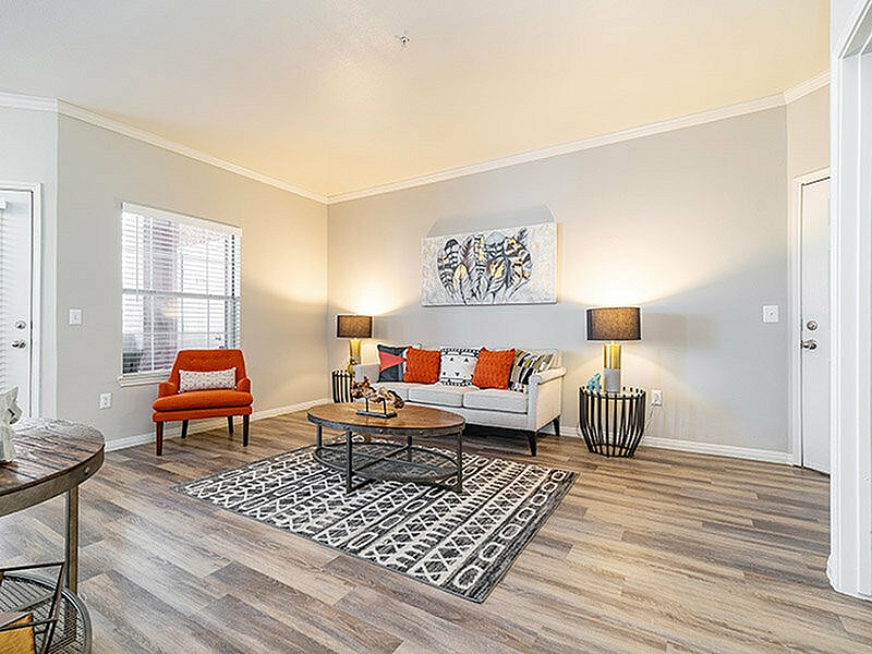 Bright and inviting living room with modern decor, featuring a cozy white sofa, vibrant orange accents, stylish coffee table, and elegant lighting on beautiful wooden flooring.