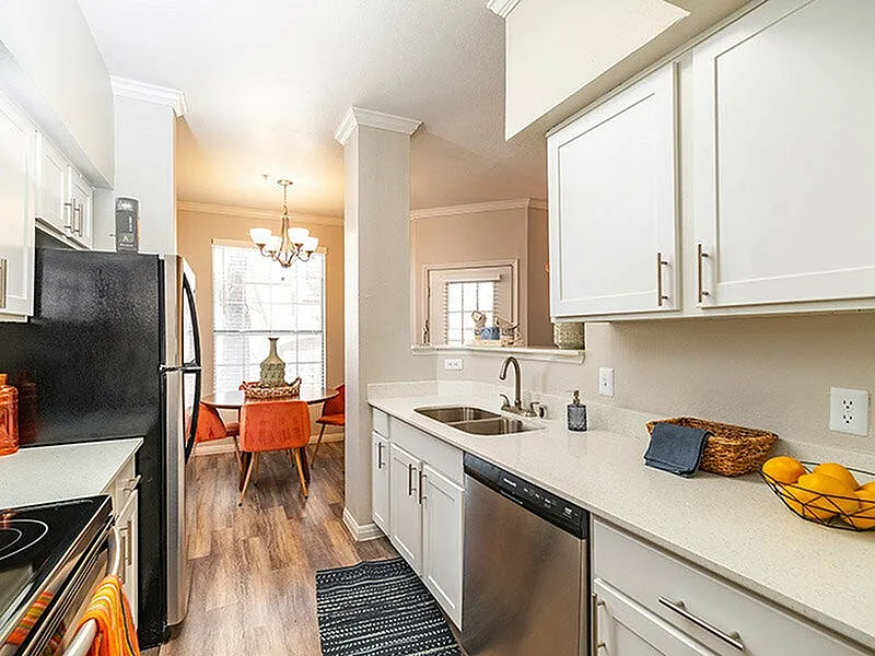 Bright and modern kitchen with sleek white cabinets, elegant countertops, and a cozy dining area with stylish orange chairs, illuminated by a chic chandelier.