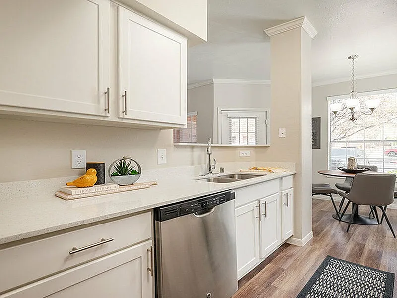 Bright, modern kitchen with sleek white cabinetry, stainless steel dishwasher, and cozy dining area with large window.