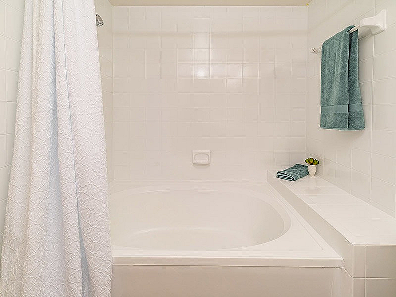 Elegant bathroom featuring a pristine white tiled bathtub with plush teal towels and a serene ambiance.