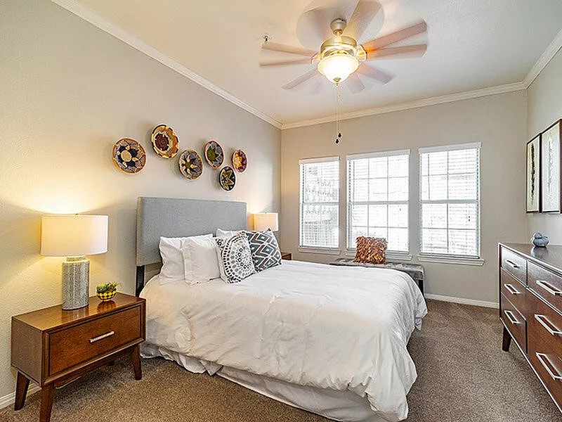 Inviting bedroom with stylish decor, modern ceiling fan, and ample natural light from large windows, creating a tranquil retreat.