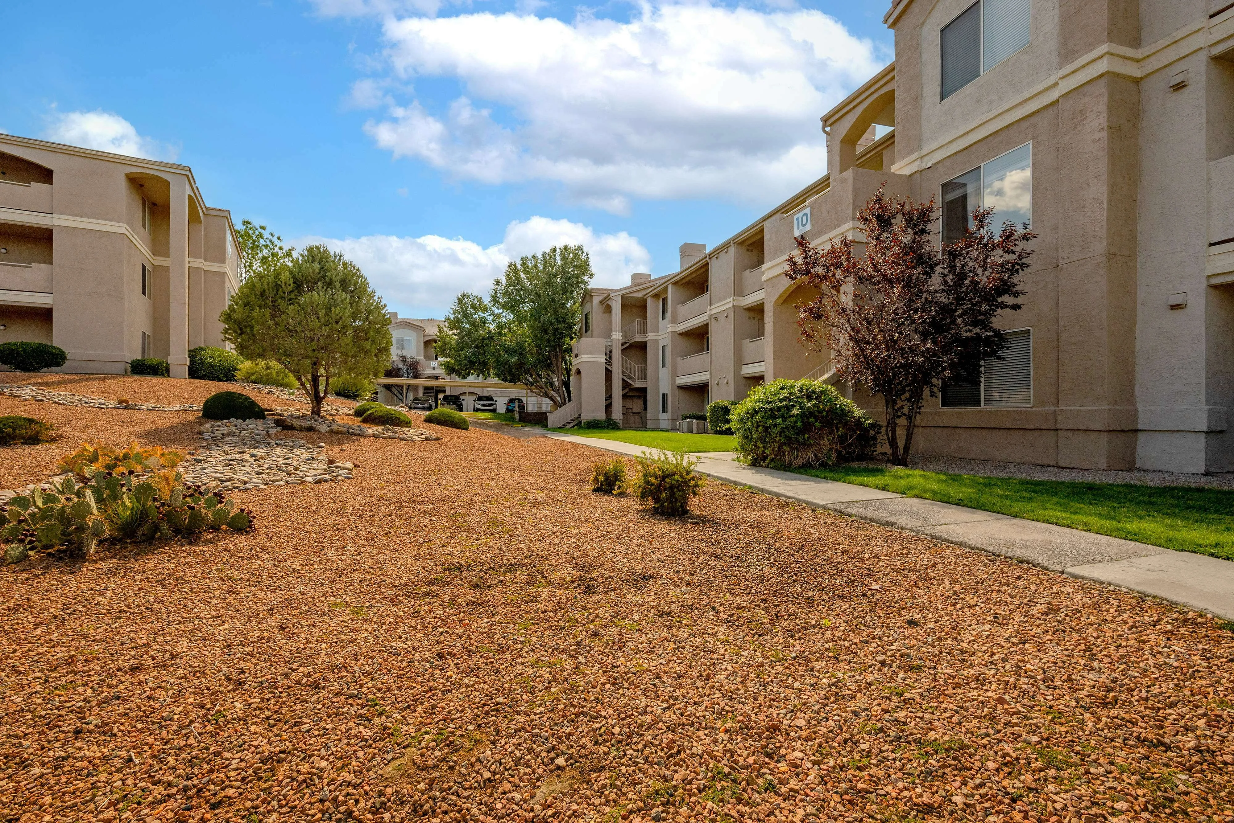 Inviting apartment complex with scenic landscaping, featuring stylish buildings under a bright blue sky, offering a harmonious living environment.