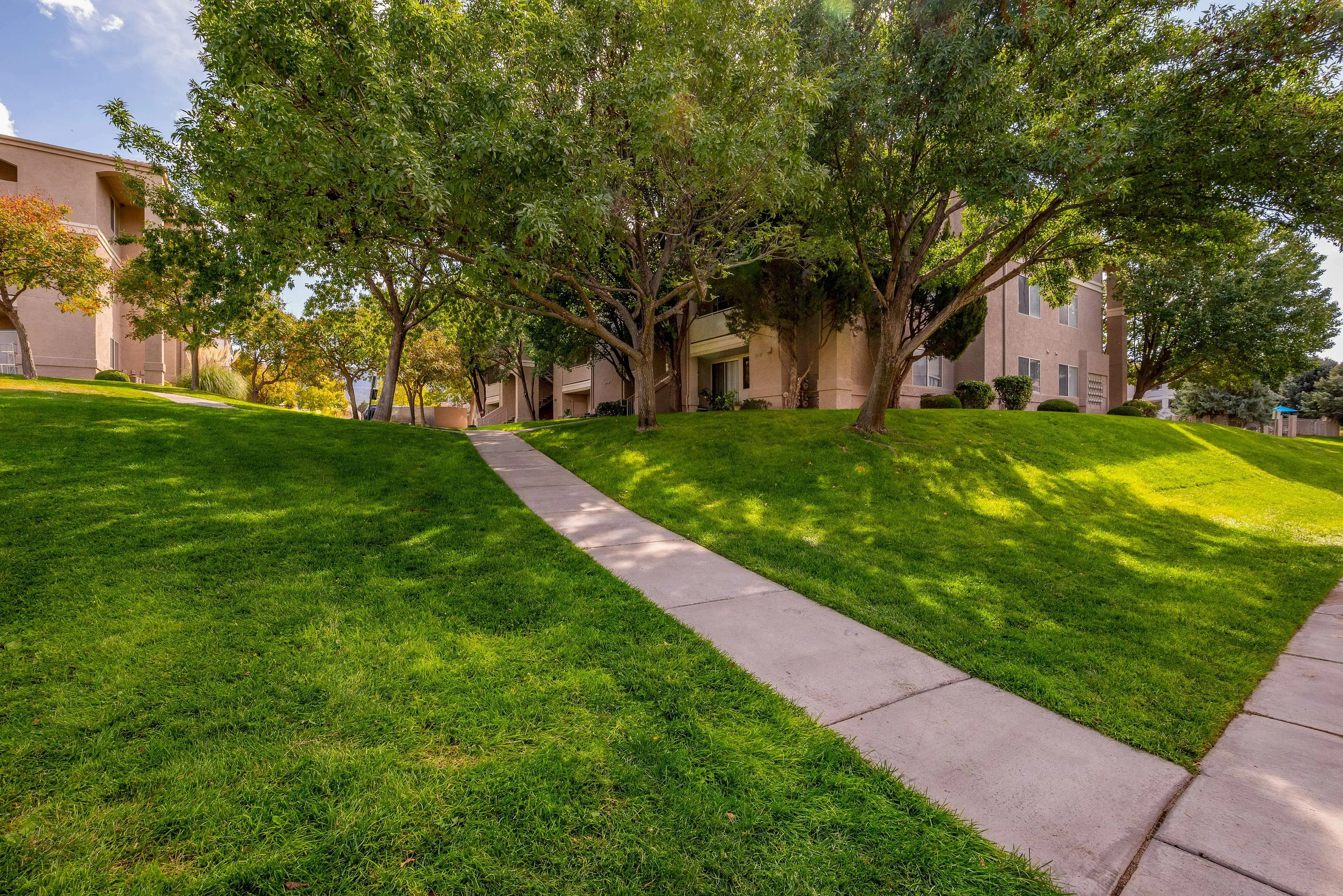 Charming apartment exterior with lush green lawns and mature trees, creating a serene and inviting pathway to your new home.
